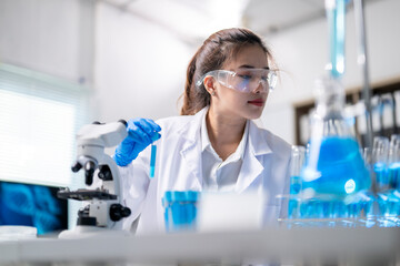 A woman in a lab coat is wearing safety goggles and holding a test tube