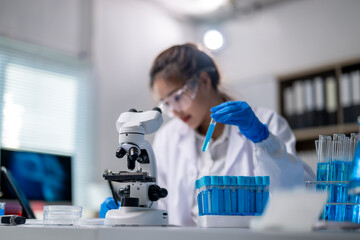 Fototapeta premium A woman in a lab coat is holding a blue liquid in a test tube