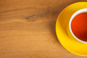 A yellow cup and saucer stands on a wooden background with black tea poured, half of a mug with space for text is visible. The concept of tea drinking, tea tradition, break. High quality photo