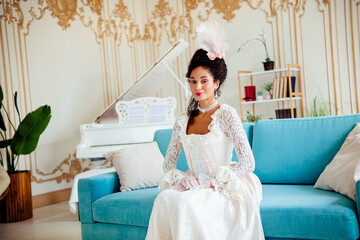 Elegant young woman in baroque-inspired dress sitting on a modern sofa