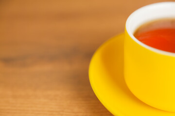 A bright yellow cup with a saucer to which fragrant tea is poured stands on the left, part of the mug is visible on a wooden background. High quality photo