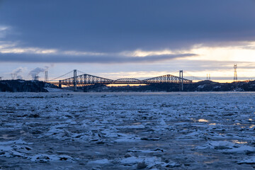 The 1970 suspension Pierre-Laporte Bridge and 1919 steel truss Quebec Bridge in silhouette during a blue hour winter sunrise on the St. Lawrence River, Cap-Rouge area, Quebec City, Quebec, Canada