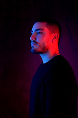 Stylish profile portrait of a confident man in moody red and blue lighting, wearing black attire against a dark background