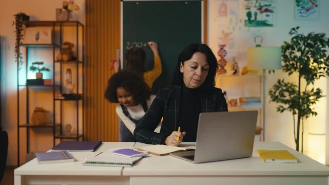 Calm female teacher works in the classroom while students run around noisily
