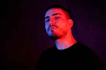 Stylish portrait of a defiant man in moody red and blue lighting, wearing black attire against a dark background