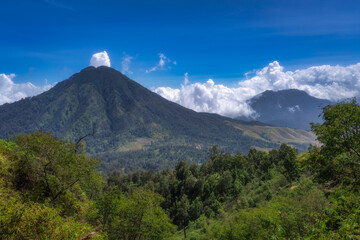 Majestic mountains tower impressively against a clear blue sky, surrounded by vibrant green foliage and fluffy white clouds, showcasing the breathtaking beauty of nature, Java, Ijen Volcano, Indonesia