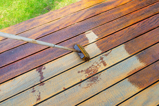 Close-up of a wooden deck being stained with a brush for protection and maintenance during a home improvement project in bright sunlight