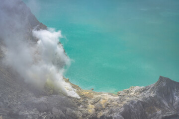 A stunning aerial vista showcasing a magnificent Ijen volcano, burning sulfur deposit releasing steam, framed by azure waters of acid lake under the radiant sunlight, East Java, Indonesia
