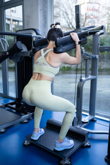 Female athlete performing hack squat exercise, strengthening leg muscles in modern fitness center,...