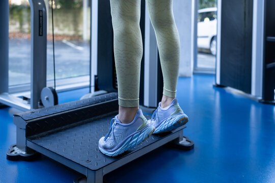 Muscular female athlete performing calf raises on exercise machine, strengthening lower leg muscles in contemporary fitness center