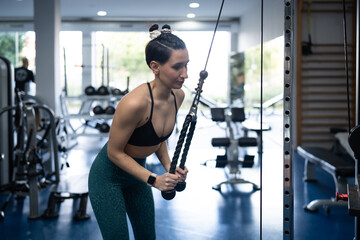 Muscular woman performing triceps pushdown on cable machine, displaying strength and fitness dedication in contemporary gym environment with focused professional technique