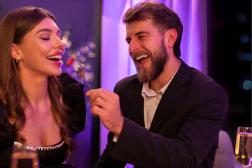 Naklejka premium Affectionate couple having dinner, man feeding his girlfriend with salad, lovers having romantic date, celebrating St. Valentine's Day or anniversary