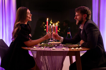 Happy lovers on romantic date in restaurant clinking champagne glasses, celebrating Valentine's day evening, side view
