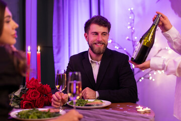 Waitress proposing wine bottle to couple, man and woman choosing beverage during romantic dinner in restaurant