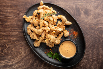 A plate of crispy fried chicken strips served with a flavorful dipping sauce. Garnished with herbs, this delicious dish is perfect for sharing or enjoying as a snack.