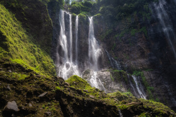 This truly majestic Tumpak Sewu Waterfall is beautifully framed by vibrant, colorful foliage, showcasing the incredible beauty of nature in a tranquil, idyllic landscape setting, East Java, Indonesia