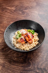 A delicious dish featuring grilled salmon, broccoli, and a savory sauce served over pearl couscous. Presented in a stylish black bowl on a wooden table, perfect for gourmet menus.