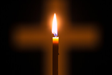 Candle is lighting and glowing through hole in shape of Christian cross among darkness. Light of faith is shining in darkness of unbelief. Concept of Christianity, religiosity and sincere faith