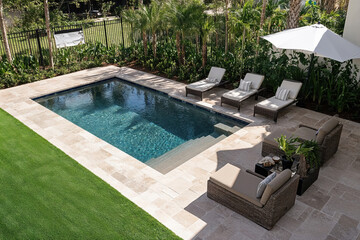 Inviting backyard oasis featuring a sparkling swimming pool, lush landscaping, and comfortable lounge area