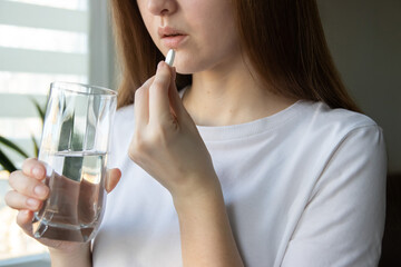 Dietary supplements. Close-up of woman taking vitamin D, vitamin C, magnesium pill with glass of...