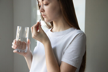 Close-up of woman taking vitamin D, vitamin C, magnesium pill with glass of water. Vitamins for women