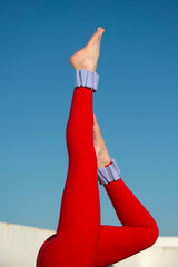 close up of womans legs in the air wearing adjustable ankle weights wearing red sports clothing, blue sky