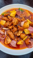 Sweet and sour pork (or chicken). Dish features battered and fried pieces of meat coated in a vibrant reddish-orange, glossy sauce, along with chunks of pineapple and onion wedges. Chinese restaurant
