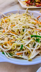 White bowl filled with stir-fried bean sprouts is the main focus. Thin strips of carrots and green onions are mixed in. The dish looks simple and fresh, likely a side dish in a Chinese Asian meal
