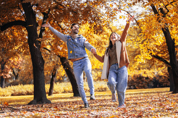 Fototapeta premium Happy couple throws leaves in the colorful park on an autumn day.
