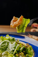 Close-up of a fork holding a shrimp and lettuce over a fresh, vibrant salad plate