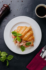 Fresh croissant sandwich with prosciutto and basil served on plate, perfect for a gourmet breakfast