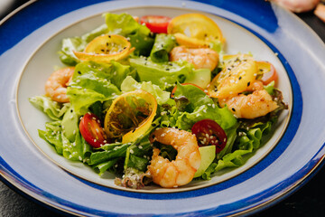 Fresh shrimp salad with cherry tomatoes, citrus slices, and sesame seeds on a vibrant blue plate