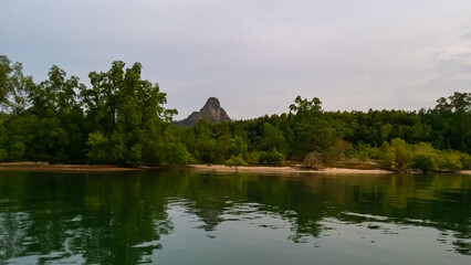 Calm body of water reflects lush green shoreline with dense trees in Kilim Geoforest Park, Langkawi Island, Malaysia, Asia. Distinctive pointed rock formation. Sense of tranquility and natural beauty