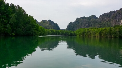 Calm river or waterway flows between steep, forested hills or cliffs in Kilim Geoforest Park on...