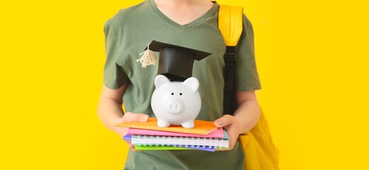 Teenage boy with savings for education and copybooks on yellow background