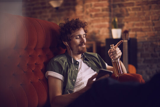 Man relaxing on couch with headphones and a smartphone in bar