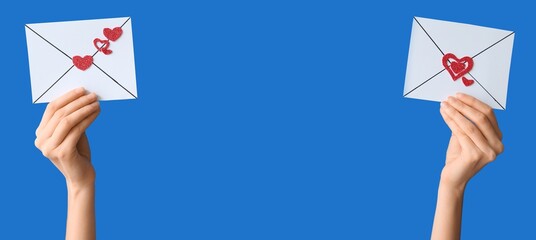 Female hands holding envelopes with hearts on blue background. Valentine's Day celebration