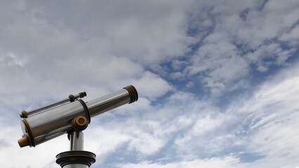 Vintage aluminum and bronze coin-operated public telescope pointing to the mostly cloudy with blue...
