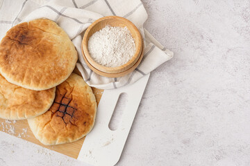 Wooden board of tasty pita bread and flour on white background