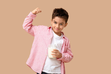 Cute little boy with mason jar of milk on beige background