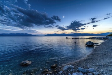 Obraz premium Noche Celestial: Evening Sky Over a Tranquil Sea with Stars, Clouds, and a Serene Blue Moon Reflection