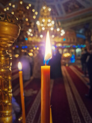 Closeup of a lit candle on the candelabra inside a Christian Orthodox church. The burning flame is sharp and bright. Religious symbol for Easter or Christmas holidays. Religion, creed and God concept