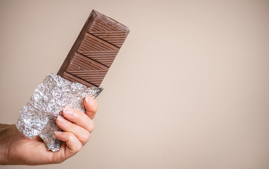 a bar of delicious chocolate in a woman's hand on a light background.