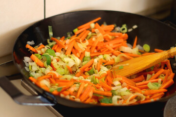 Sauteing chopped leek and carrot slices in a wok. Selective focus.