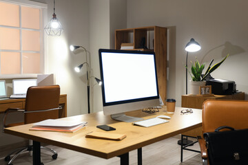 Workplace with blank computer monitor in office at night