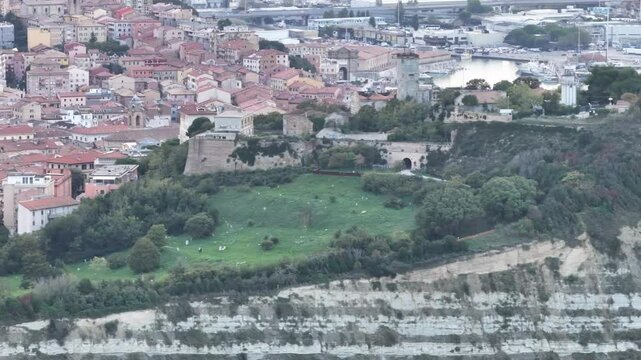 A video highlighting the dramatic cliffs of Ancona, covered in greenery, with historic buildings, a lighthouse, and the harbor in the background, showcasing the area's unique blend of nature and archi