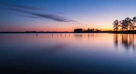 Obraz premium Tranquil Lake at Dusk with Silhouetted Trees and Clear Sky