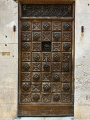 Ornate wooden door with intricate carvings in a historic setting. A detailed wooden door with floral carvings and decorative ironwork, set in an aged stone wall.