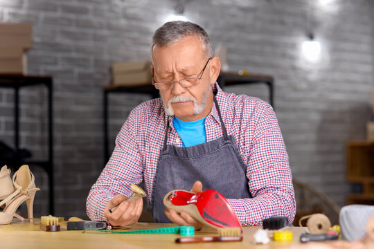 Mature shoemaker repairing broken heel at table in workshop - Powered by Adobe