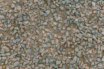 Granite gravel scattered on soil. Rough crushed stones in varied colors and shapes. Top view of natural rocky surface for paths or backgrounds.